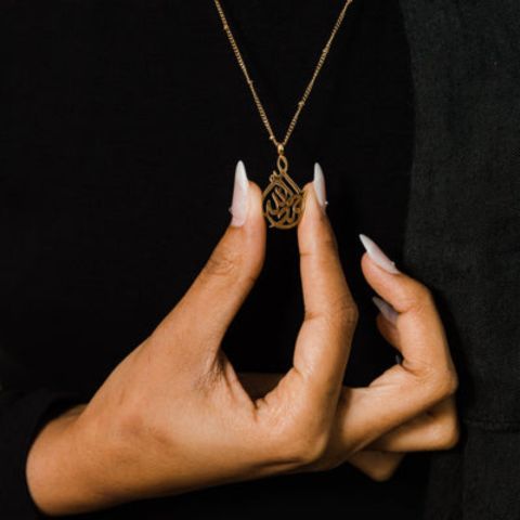 A cradle-shaped silver necklace featuring Arabic calligraphy of the word 