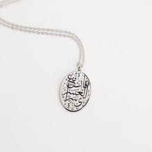 A silver oval pendant necklace featuring Arabic calligraphy of the verse 