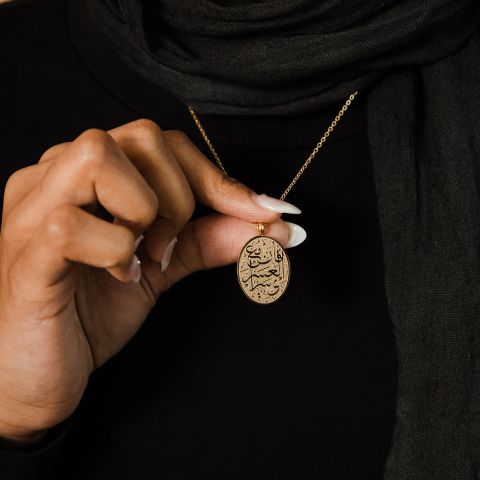 A silver oval pendant necklace featuring Arabic calligraphy of the verse 