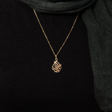 A cradle-shaped silver necklace featuring Arabic calligraphy of the word 