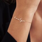 A delicate romantic script heart bracelet in 18k gold-plated sterling silver, worn on a woman's wrist.