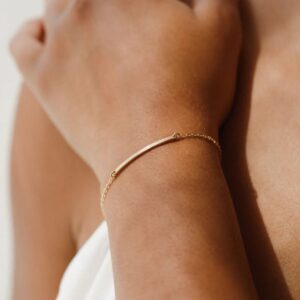A minimalist personalized bar bracelet in 18k gold-plated sterling silver, engraved with the name 'Ava', worn delicately on a wrist.