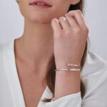 A signature custom engraved bangle in 18k gold-plated sterling silver, worn on a woman's wrist and engraved with the name 'Eleanor'.