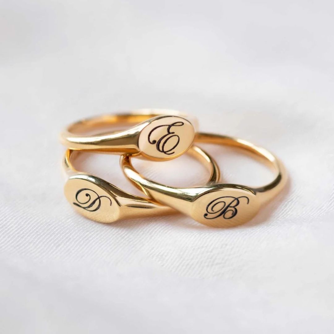 A classic personalized oval signet ring in 18k gold-plated sterling silver, engraved with a 'J' monogram and worn on a finger.