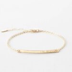 A minimalist personalized bar bracelet in 18k gold-plated sterling silver, engraved with the name 'Ava', worn delicately on a wrist.