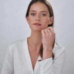 A signature custom engraved bangle in 18k gold-plated sterling silver, worn on a woman's wrist and engraved with the name 'Eleanor'.