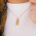 "With Hardship Comes Ease" verse bar necklace in 18k gold-plated sterling silver, showing the vertical pendant with Arabic calligraphy.