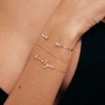 A delicate romantic script heart bracelet in 18k gold-plated sterling silver, worn on a woman's wrist.