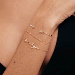 A delicate romantic script heart bracelet in 18k gold-plated sterling silver, worn on a woman's wrist.