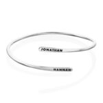 A signature custom engraved bangle in 18k gold-plated sterling silver, worn on a woman's wrist and engraved with the name 'Eleanor'.
