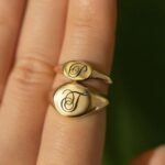 A classic personalized oval signet ring in 18k gold-plated sterling silver, engraved with a 'J' monogram and worn on a finger.