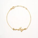 A delicate romantic script heart bracelet in 18k gold-plated sterling silver, worn on a woman's wrist.
