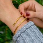 A signature custom engraved bangle in 18k gold-plated sterling silver, worn on a woman's wrist and engraved with the name 'Eleanor'.