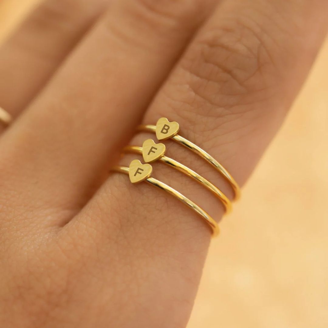 A dainty personalized heart initial 'A' ring in 18k gold-plated sterling silver, worn on a woman's finger.