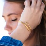 A signature custom engraved bangle in 18k gold-plated sterling silver, worn on a woman's wrist and engraved with the name 'Eleanor'.