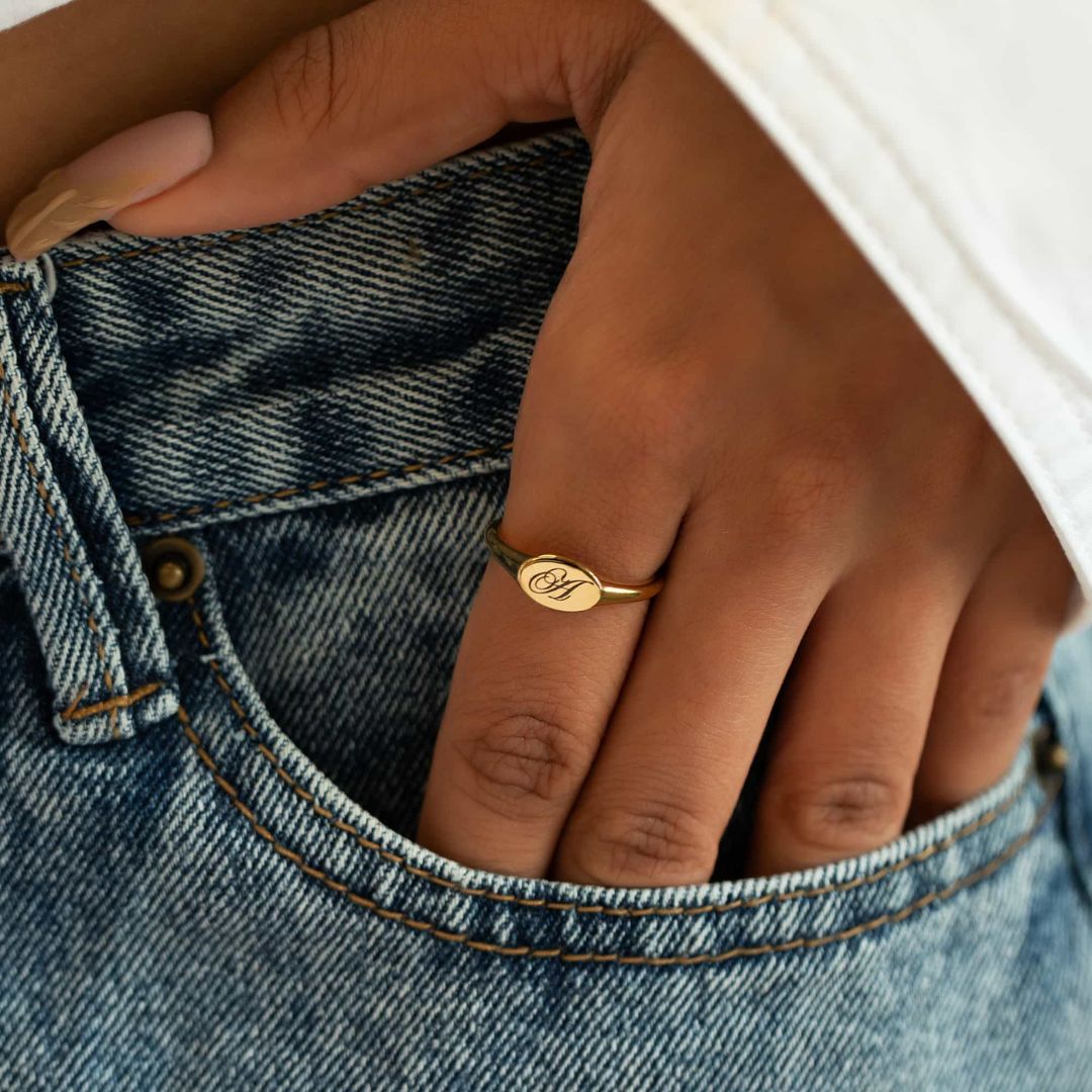 A classic personalized oval signet ring in 18k gold-plated sterling silver, engraved with a 'J' monogram and worn on a finger.
