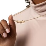 A 'Maktub' raised calligraphy necklace in 18k gold-plated sterling silver, showing the 3D effect of the Arabic script on the round medallion.