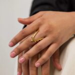 A woman's hand wearing the Kinetic Orbiting Sphere Ring in 18k gold-plated sterling silver, showing the moving bead on the elegant double band.