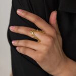 A woman's hand wearing the Kinetic Orbiting Sphere Ring in 18k gold-plated sterling silver, showing the moving bead on the elegant double band.