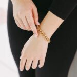 A woman's wrist wearing the bold Cuban link bracelet in 18k gold-plated sterling silver, showing the chunky, interlocking design.