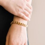 A woman's wrist wearing the bold Cuban link bracelet in 18k gold-plated sterling silver, showing the chunky, interlocking design.