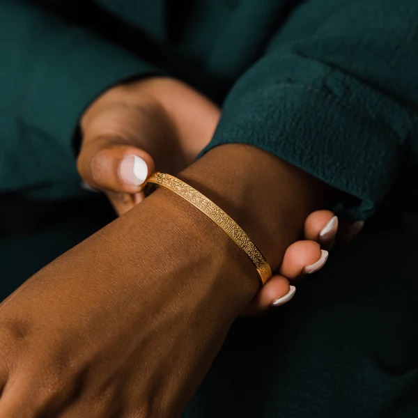 A wide Ayatul Kursi cuff bracelet in 18k rose gold-plated sterling silver, showing the intricate Arabic engraving of The Throne Verse on a woman's wrist.