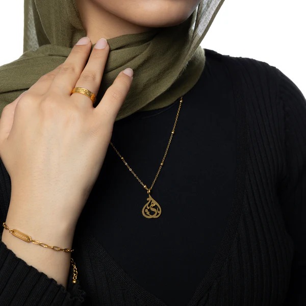 Model wearing the gold-plated sterling silver 'My Sister' Arabic calligraphy necklace (Ukhti) against a neutral background, showcasing its delicate chain and elegant script.