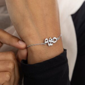 "With Hardship Comes Ease" verse bracelet in 18k gold-plated sterling silver, worn on a woman's wrist, showing the engraved Arabic bar.