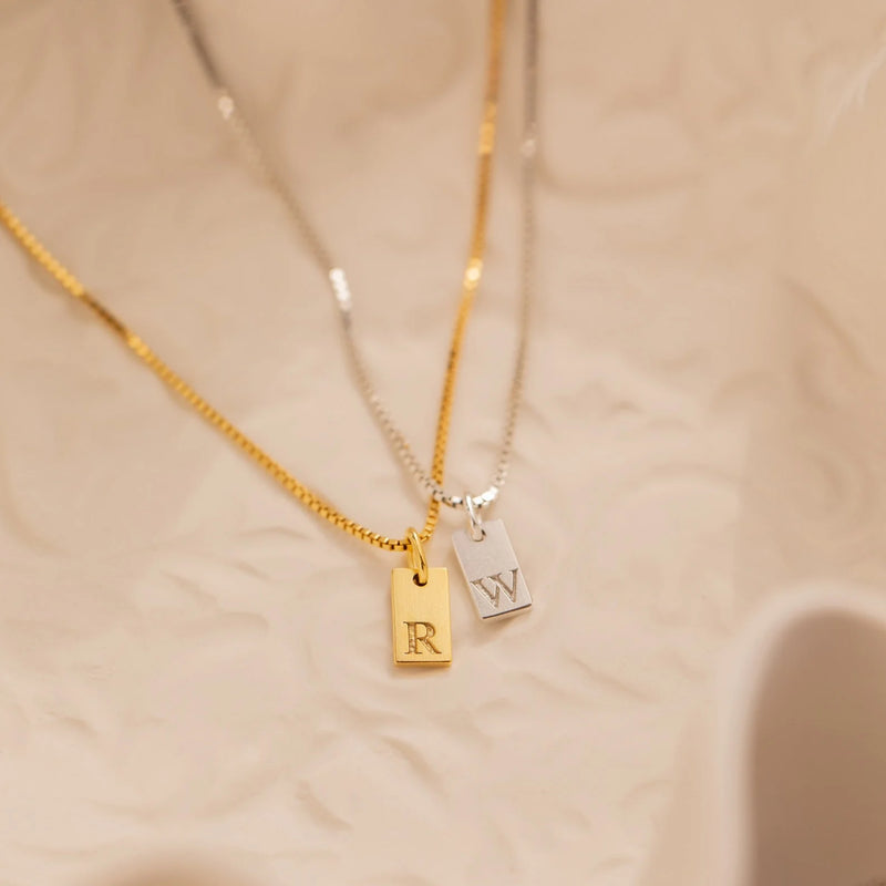 Signature initial 'K' tag necklace in 18k gold-plated sterling silver, hanging from a delicate chain against a neutral background.